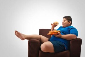 A fat boy sitting on a sofa and eating